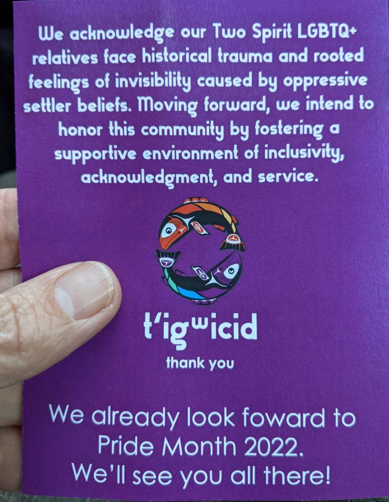 Picture of a flyer for the Swinomish Indian Community Two Spirit gathering on purple paper, held by my fingers. 