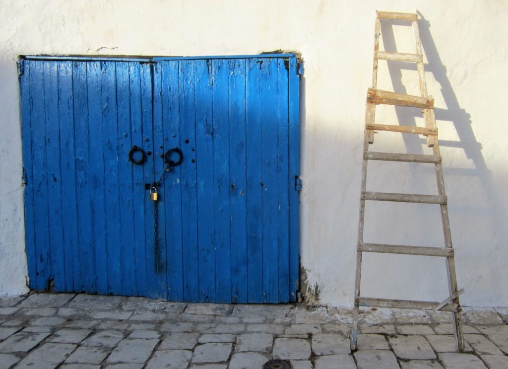 Blue door locked with a ladder leaned against the wall to the right of the door. 