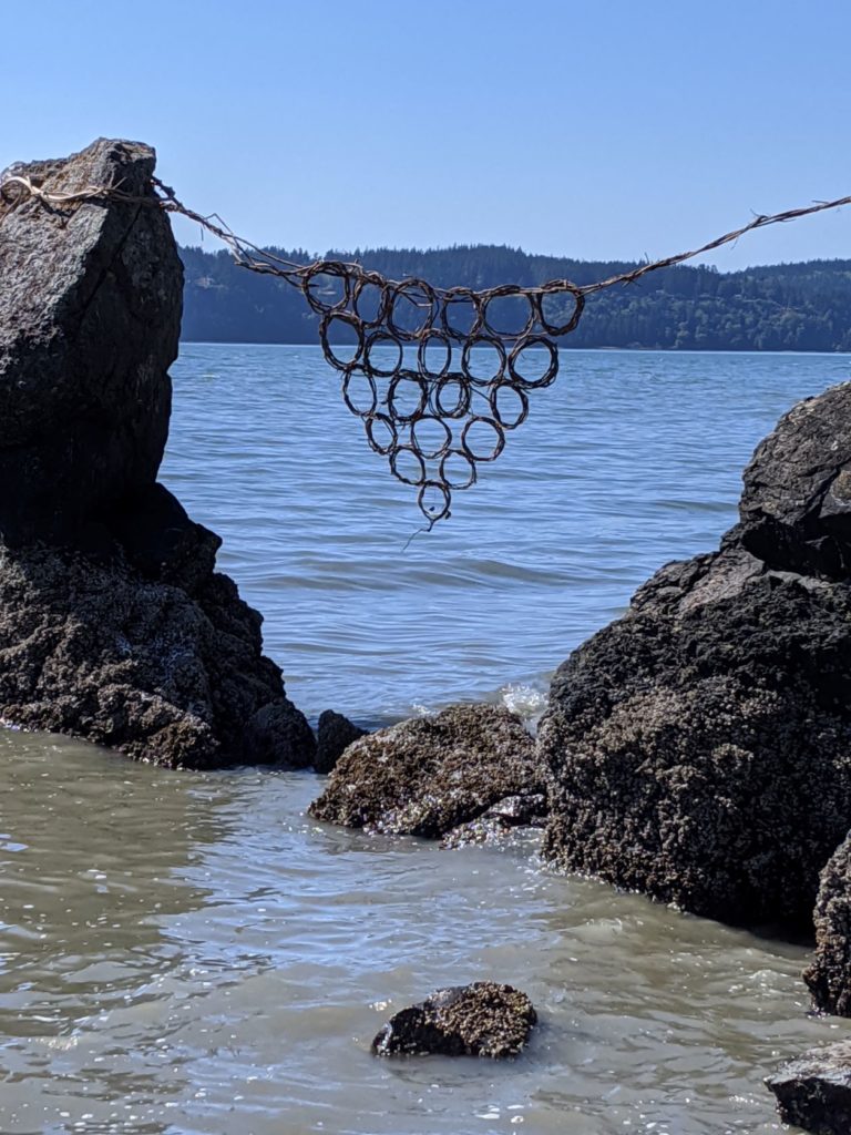 Two large rocks in a bay with a macrame bridge of circles connecting the two. 