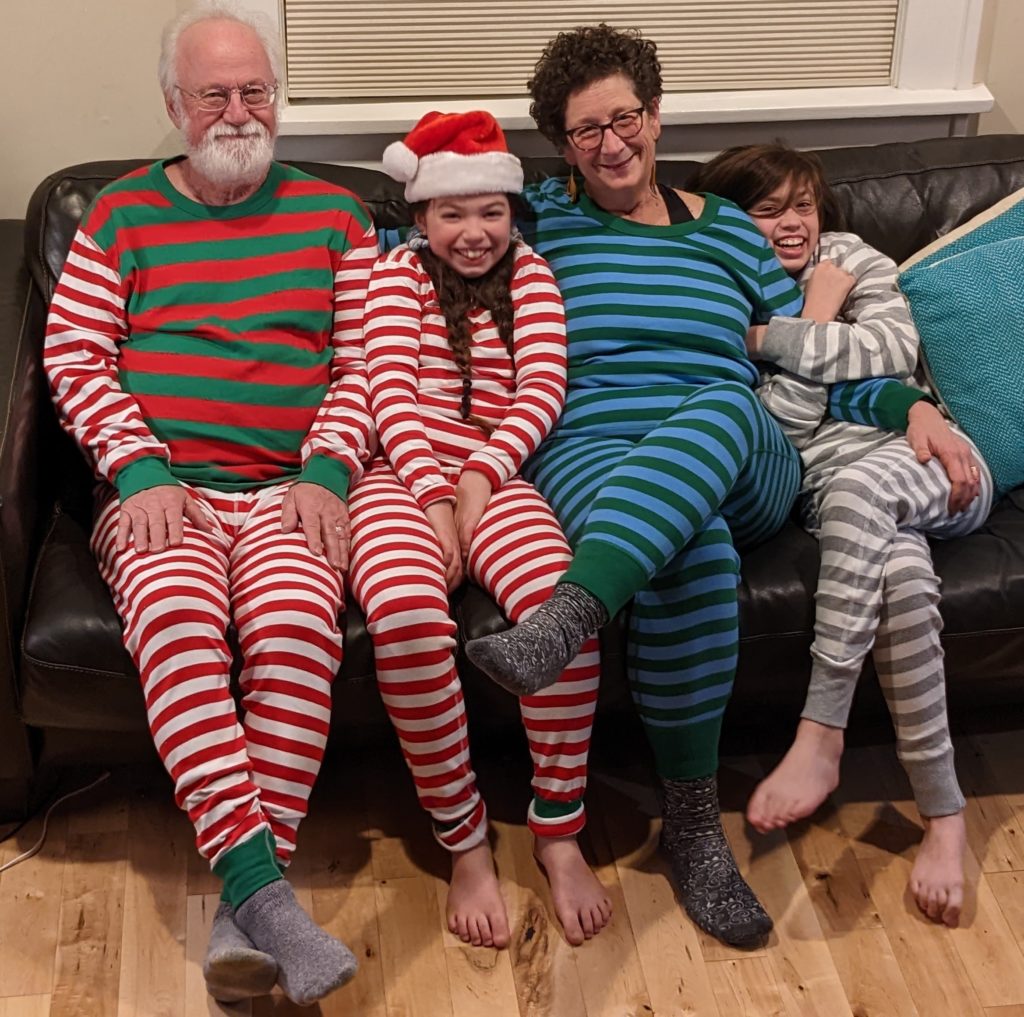 Larry White, Grandperson 2, Nancy White and Grandperson 1 sitting on couch in striped holiday PJs. 